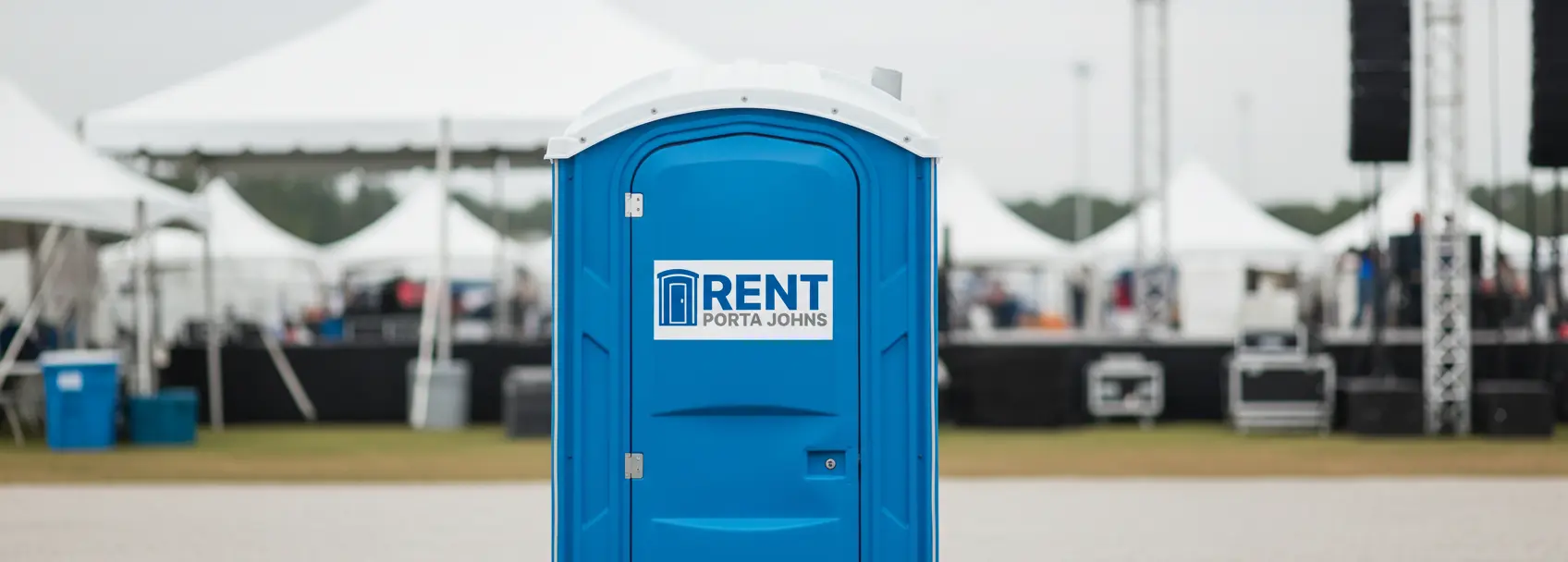 Blue portable restroom with Rent Porta Johns logo set up at an outdoor event site